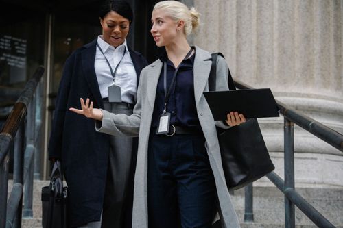 Free Cheerful multiethnic female colleagues wearing formal clothes going downstairs on stone building and chatting Stock Photo