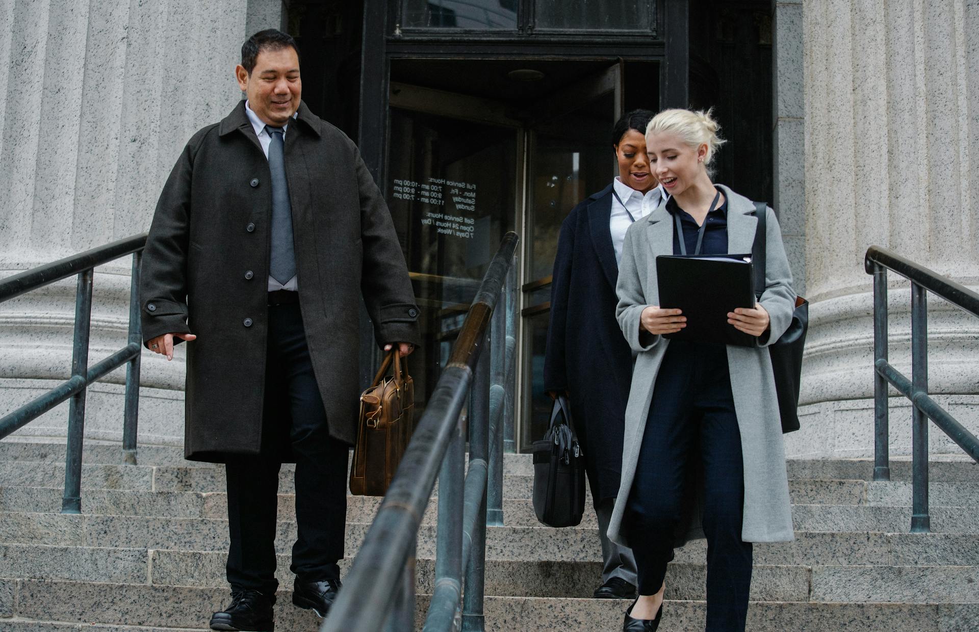 Low angle of positive multiethnic colleagues in formal clothes going down stairs of office building and smiling after successful working day