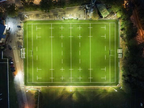 Aerial view of green well groomed illuminated rugby field located at roadside in countryside at night