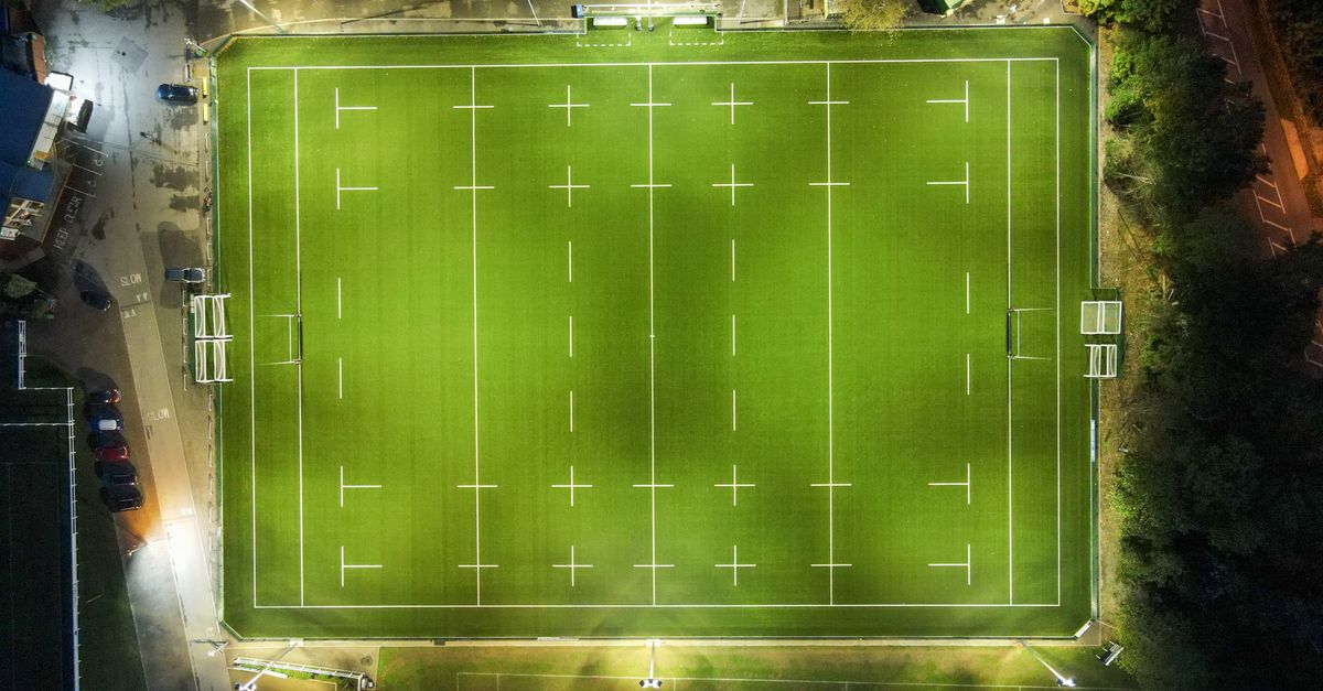Aerial view of green well groomed illuminated rugby field located at roadside in countryside at night