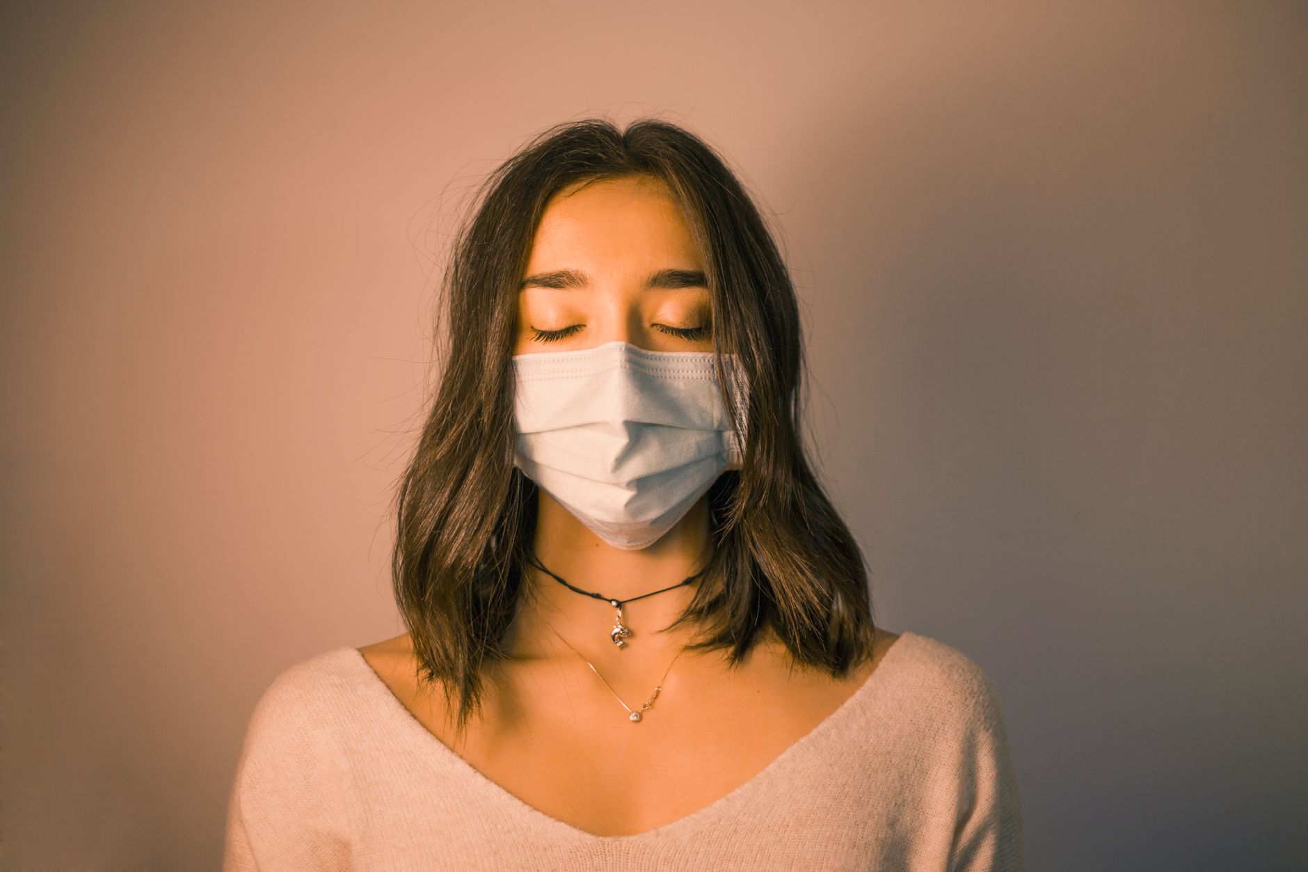 mebendazole for long covid brain fog recovery — Unemotional young female in protective face mask standing with eyes closed against dark pink wall