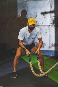 Athletic man in gym performing intense battle rope exercise with focus and determination.
