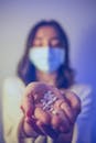 Woman in face mask showing medical pills on palm