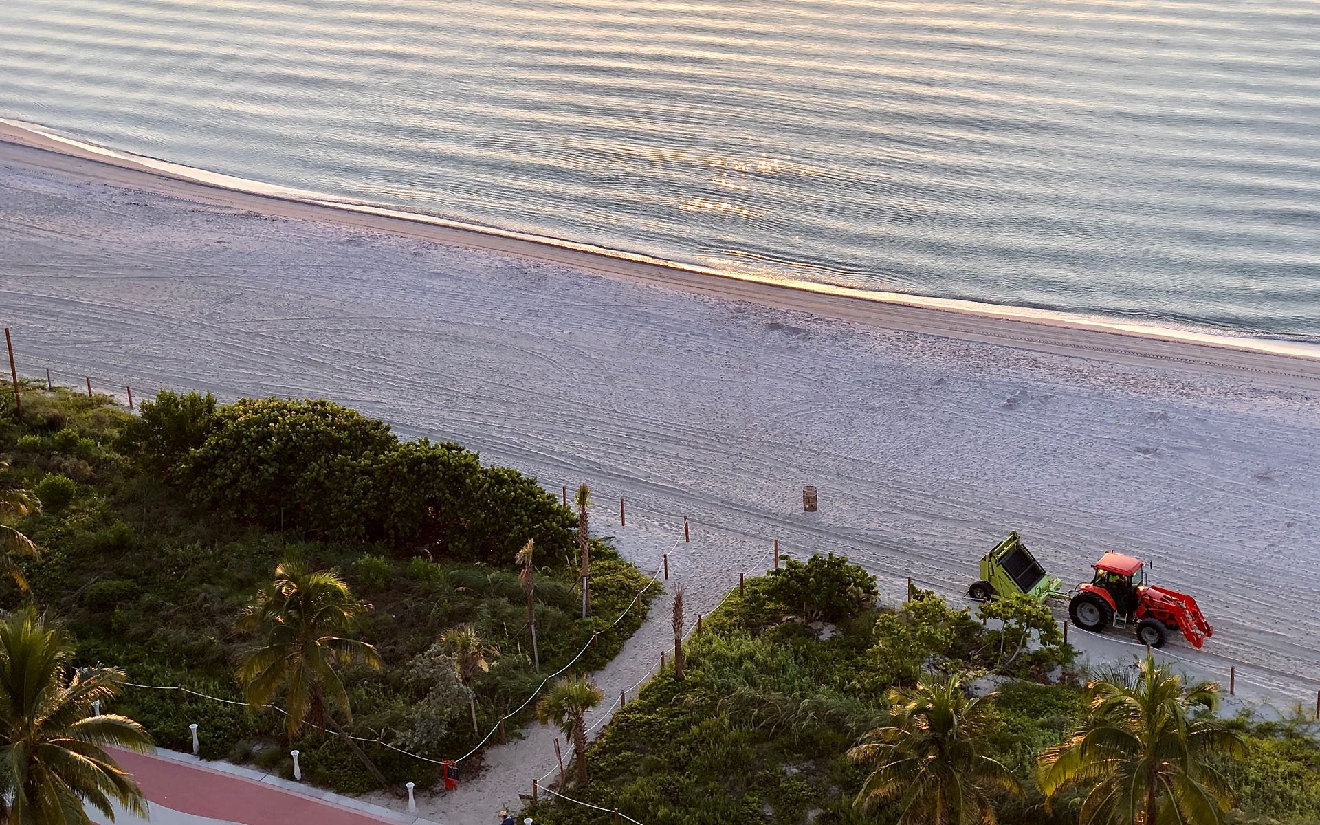 Drone shot of Miami Beach's coastline during sunrise with a lush path, sandy shore, and ocean waves.