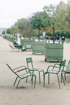 Four green metal chairs in a serene Paris park under cloudy skies.