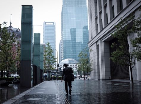 东京的现代街道上，一名商人撑着伞走在雨中