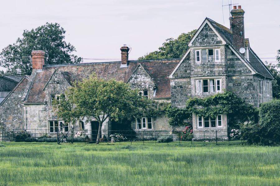 A stone cottage with a large lawn and old trees