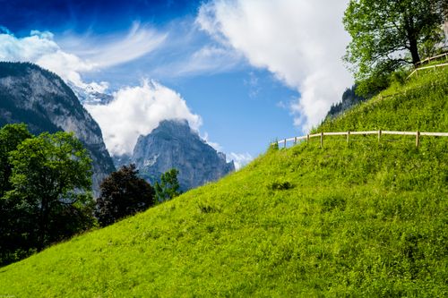Free Breathtaking landscape featuring a vibrant green hillside against a majestic mountain backdrop with blue skies. Stock Photo