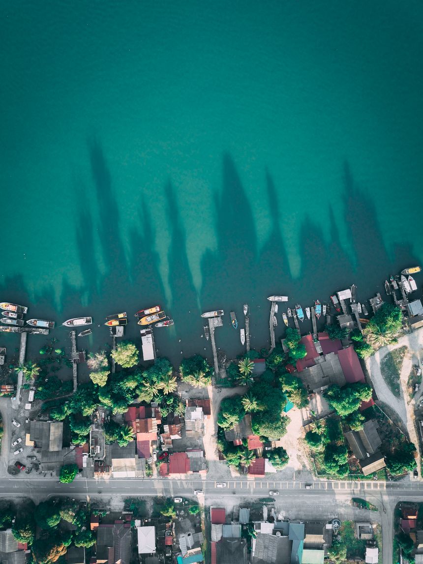Drone view of a calm sea and shoreline town with piers and moored boats — photo by Pok Rie on Pexels