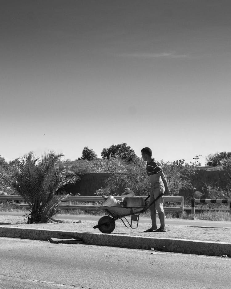 Black And White Photo Of A Man Pushing A Wheelbarrow