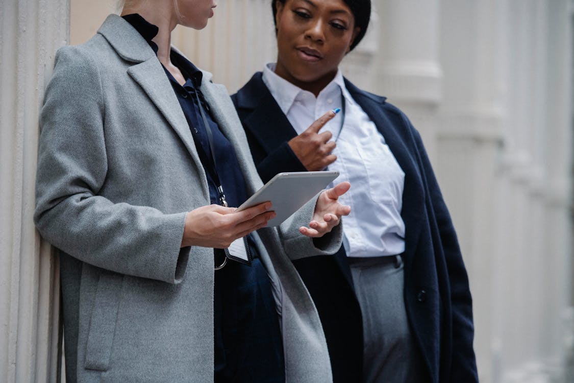 Collègues Féminines Multiraciales Concentrées à L'aide De Tablette Tout En Discutant Du Projet Sur La Rue