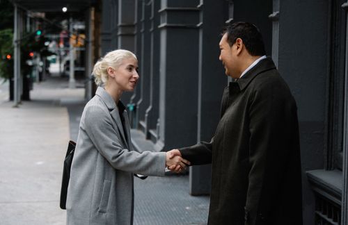 Free Side view of cheerful stylish diverse coworkers in elegant coats shaking hands and looking at each other on street Stock Photo