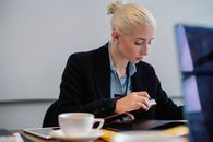 办公室里，一位穿着正式服装的年轻女商人拿着杯子，在桌旁沉思地检查文件