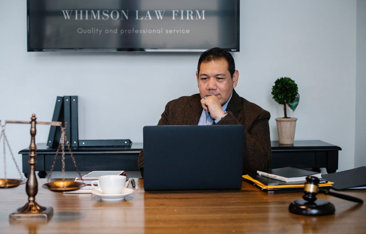 Free Serious ethnic mature man in formal outfit working with netbook at table with gavel Stock Photo