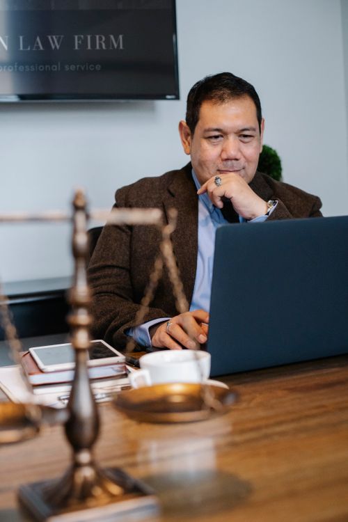 Free Cheerful ethnic legislator in formal outfit working with netbook at table with scales of justice and tablet Stock Photo