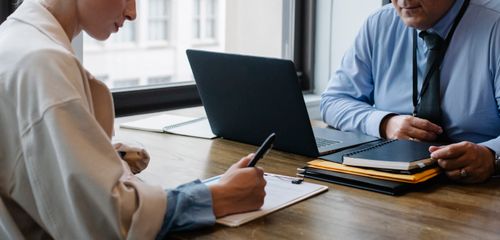 Free Crop faceless colleagues in formal clothes sitting at table with laptop and folder and signing documents while working together Stock Photo