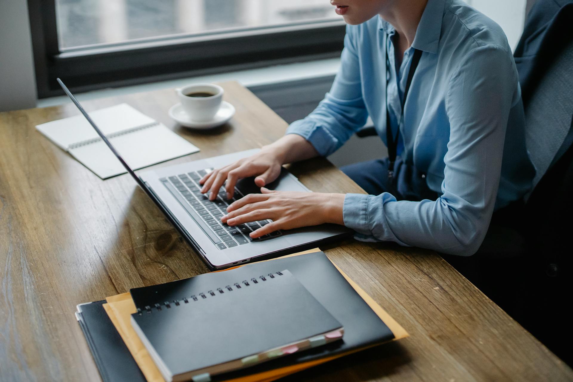 Person In Blue Long Sleeve Shirt Using Macbook Pro On Brown Wooden Table