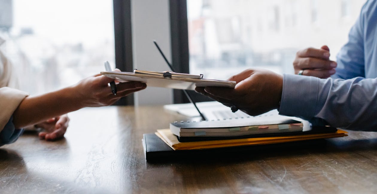 Free Crop anonymous ethnic woman passing clipboard to office worker with laptop during job interview Stock Photo