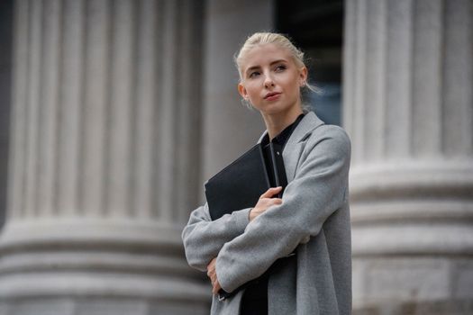 一位自信的女商人穿着灰色外套，拿着文件夹站在户外
