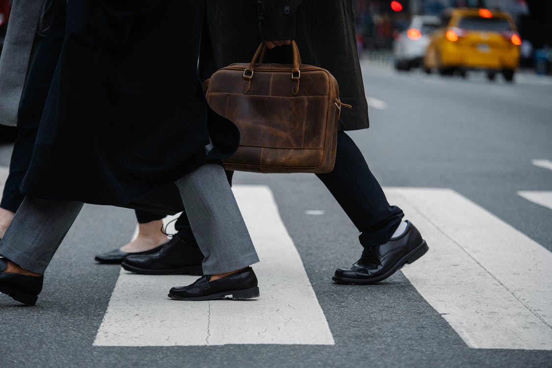 Side view of crop unrecognizable coworkers in formal wear with leather briefcase crossing urban road