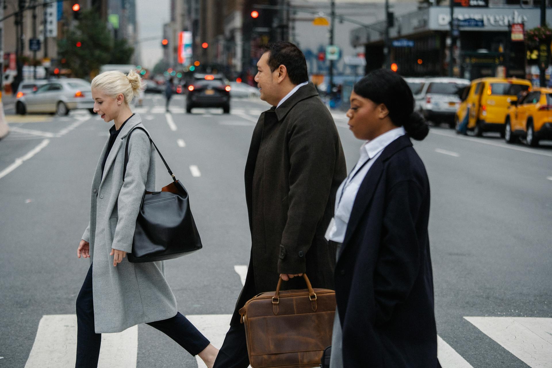 Three businesspeople confidently cross a busy city street at a crosswalk.