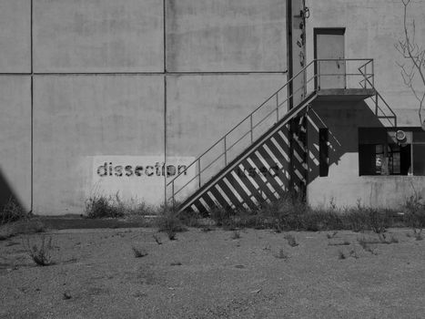 Monochrome image of an industrial building with stairs casting shadows, text 'dissection' visible.