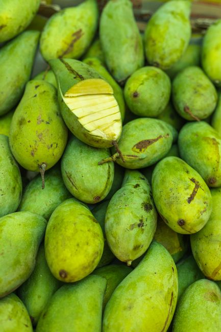 A halved unripe green mango on a cutting board showing its firm pale green-white flesh next to thin julienned strips tossed with chili and lime for a salad.