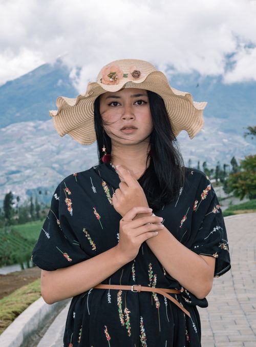 Free Portrait of a woman wearing a straw hat with mountains in the background in Indonesia. Stock Photo