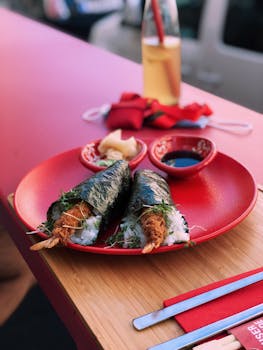 Two sushi temaki rolls on a vibrant red plate with soy dipping sauce, perfect for outdoor dining.
