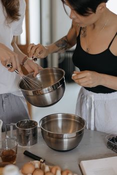Two women preparing food with mixing bowls and whisk in a modern kitchen.
