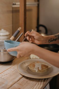 一个人在舒适的厨房里，将奶油倒在新做的煎饼上