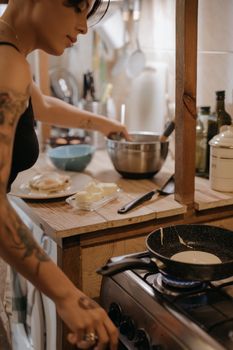 Woman with tattoos cooking pancakes in a cozy kitchen, capturing a warm and homey atmosphere.