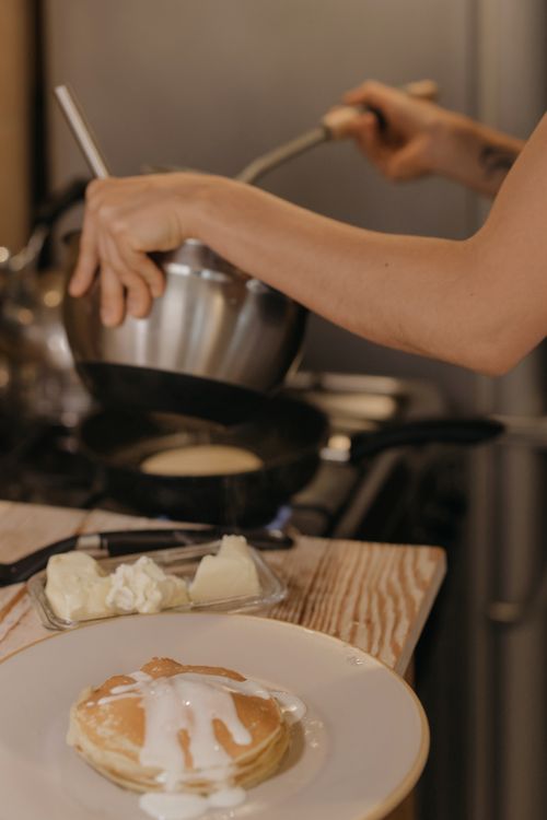 Free A person preparing pancakes on a stovetop, showcasing home cooking with syrup and butter. Stock Photo