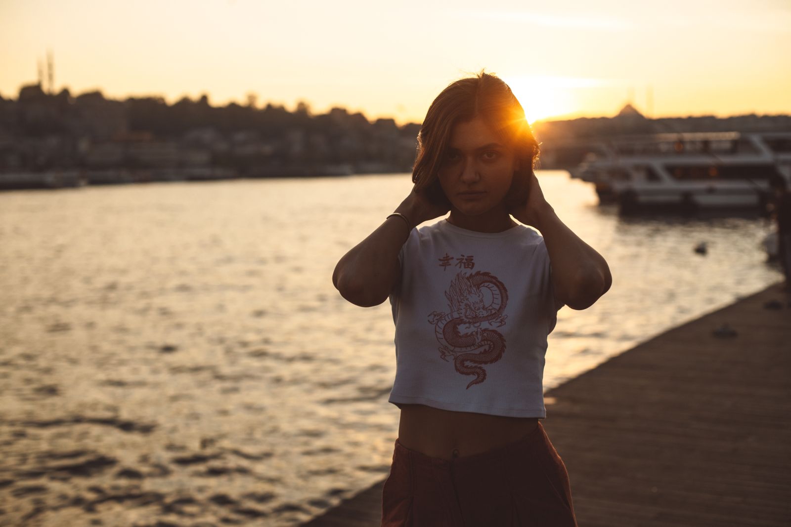 Woman with hands in her hair standing on a waterfront pier at golden sunset