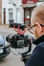 Crop anonymous professional videographer recording video on camera on street
