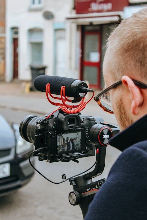 Crop anonymous professional videographer recording video on camera on street