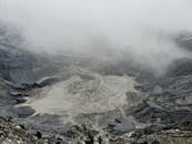 From above severe view of rough volcanic crater with hot foamy water and rocky peaks covered with dense mysterious haze