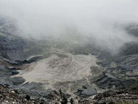 From above severe view of rough volcanic crater with hot foamy water and rocky peaks covered with dense mysterious haze