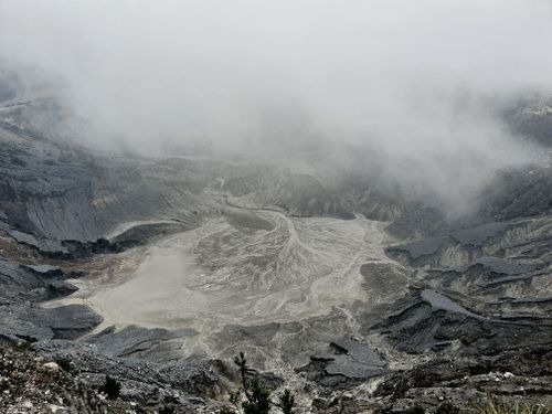 Free From above severe view of rough volcanic crater with hot foamy water and rocky peaks covered with dense mysterious haze Stock Photo