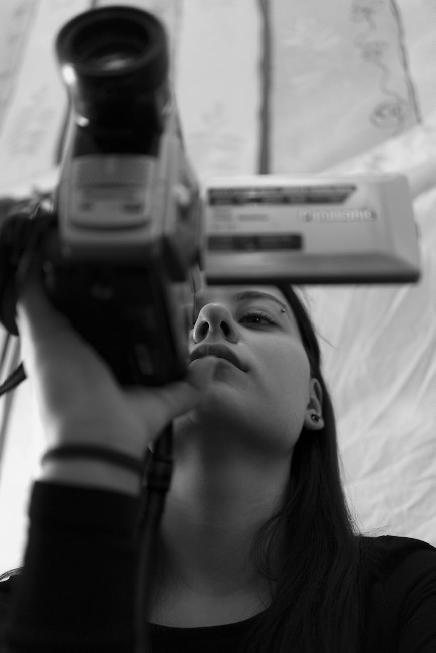 Young woman using a camcorder indoors, focusing intently. Black and white.