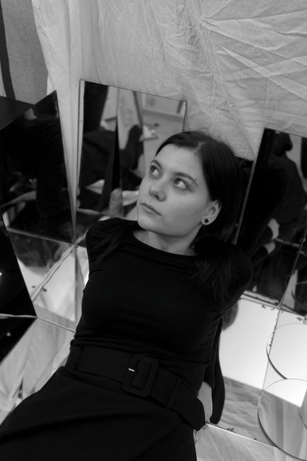 From above of black and white calm young lady sitting near mirrors in studio and looking away