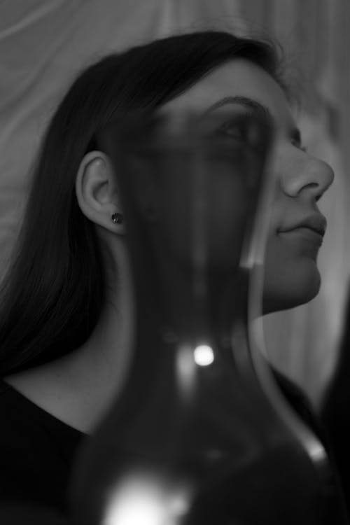 Calm young lady in dark room near glass vase