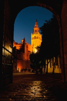 Stunning view of La Giralda Tower in Sevilla illuminated at night through an archway.