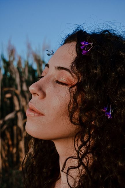 Side view of crop young female with closed eyes and flowers in curly hair under blue sky in evening