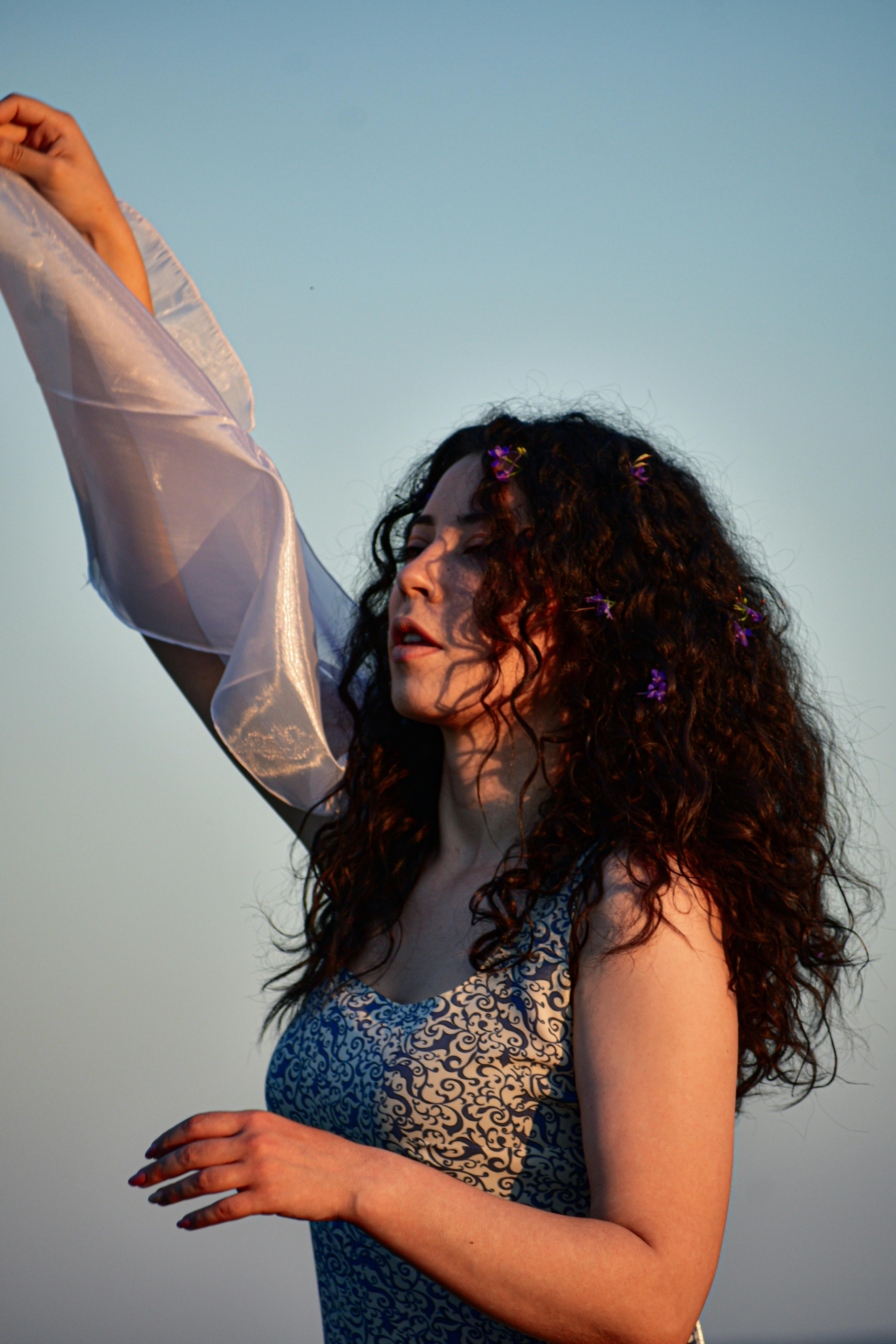 Young contemplative female in ornamental apparel looking away with raised arm in twilight