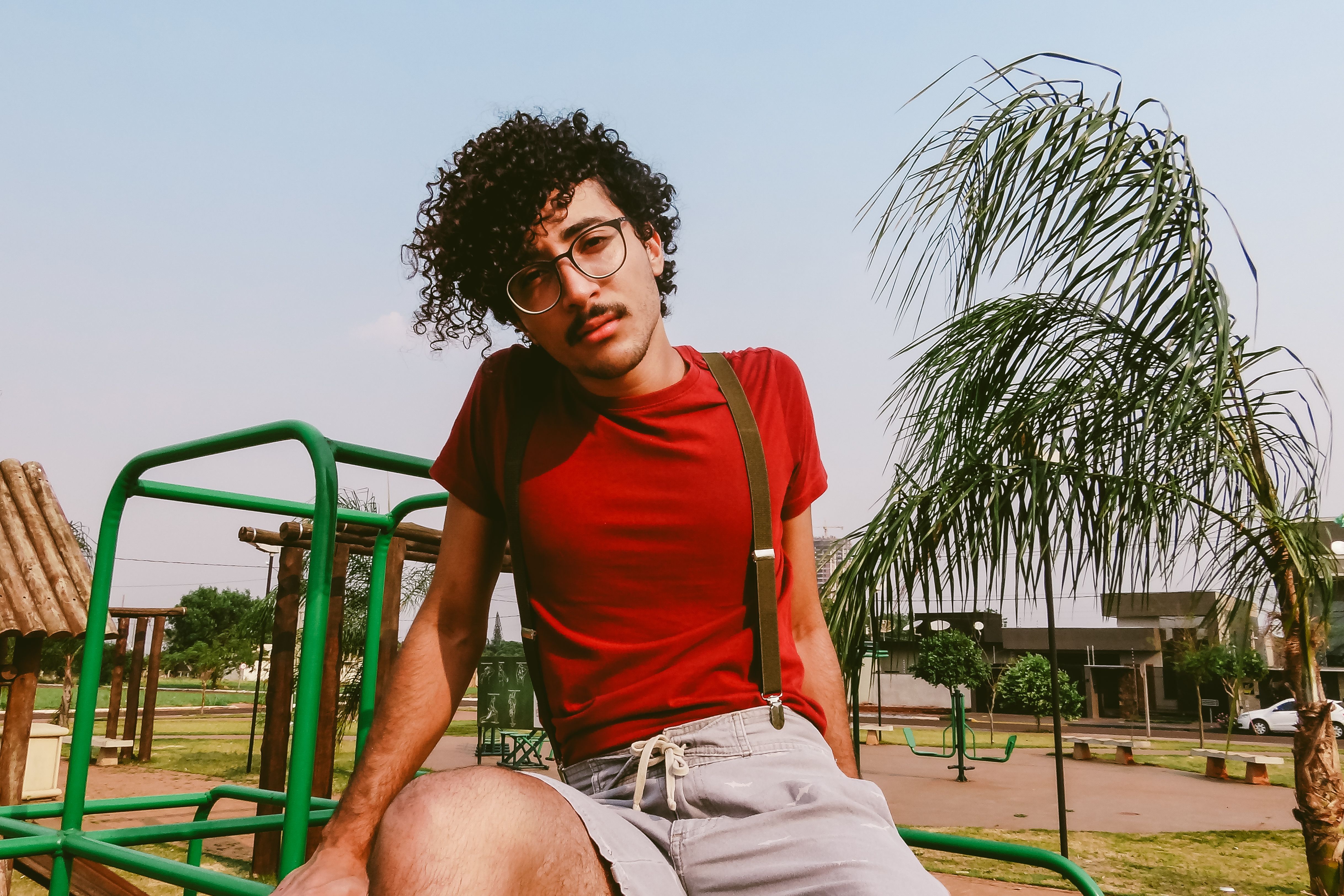 Young man in glasses posing confidently in a park setting with stylish casual attire.