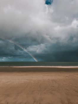 阴沉的天空中，一道令人惊叹的彩虹映照着宁静的海滩，这景象非常适合自然和旅游主题