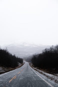 Scenic winter road in Norway, surrounded by mountains and snow-covered landscape.