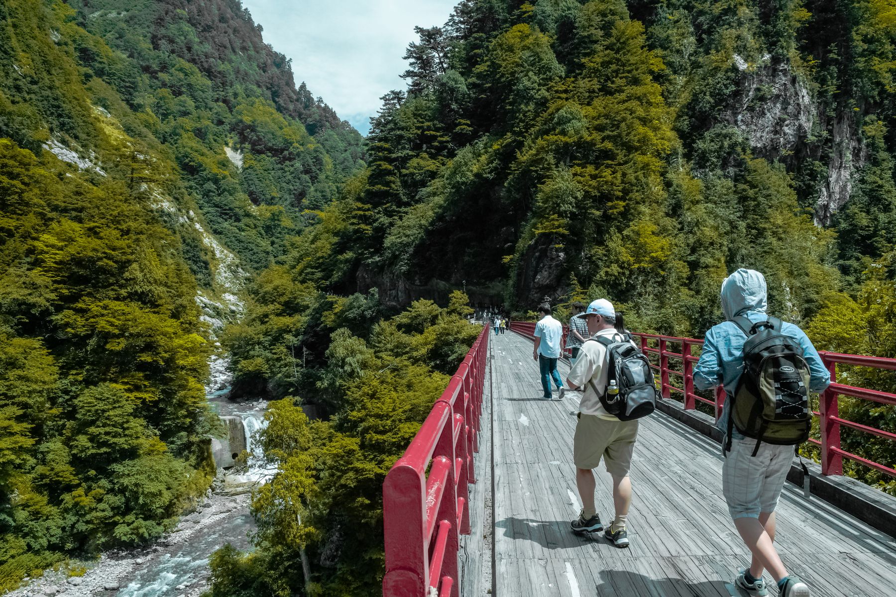 Hikers crossing a red footbridge over a mountain stream