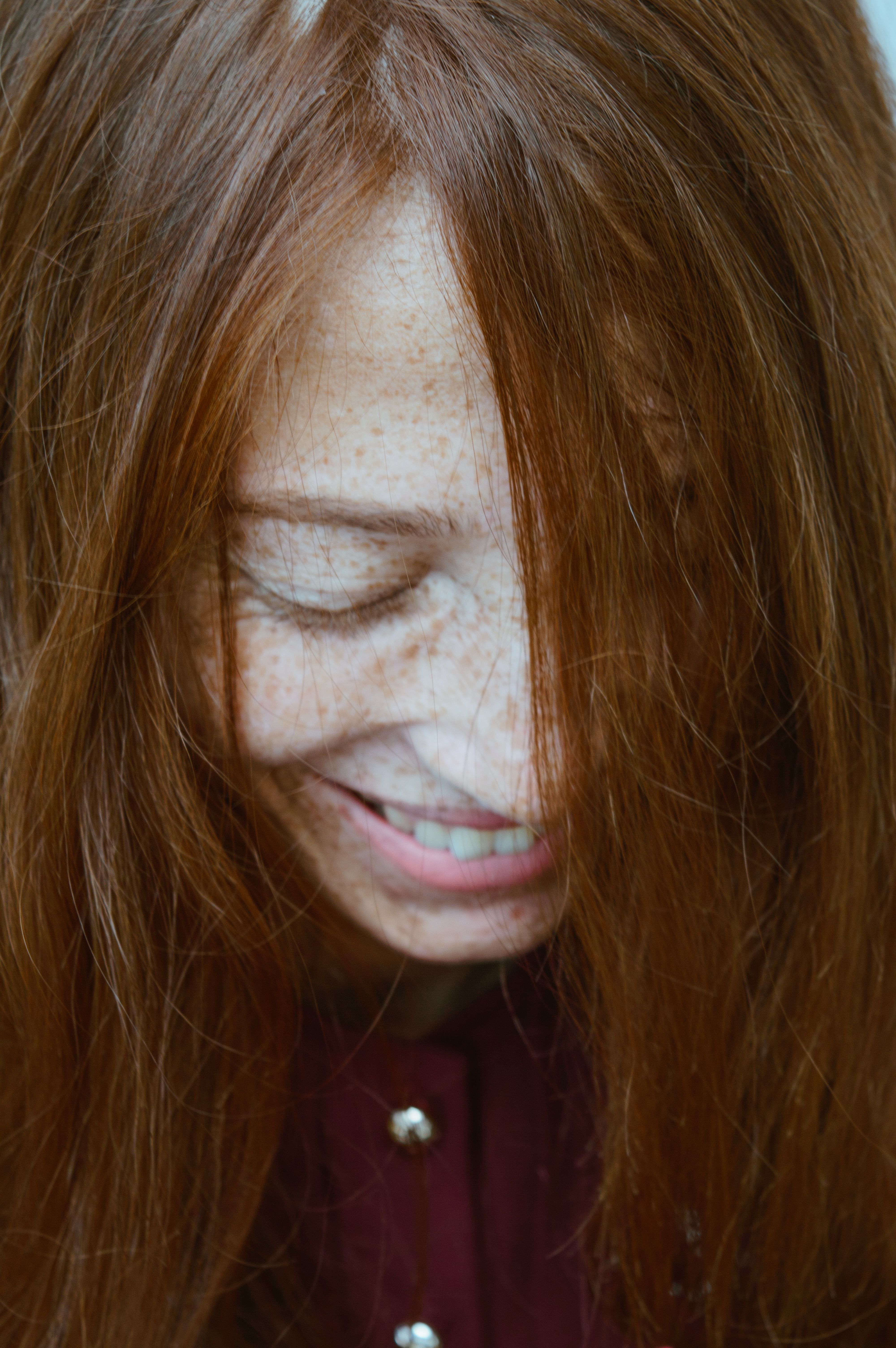 High angle of crop young happy lady with ginger hair and freckles smiling and looking down
